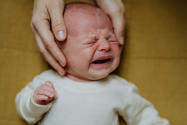 Close-up of parent stroking his crying baby lying in a bed.