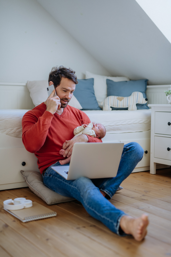 Father holding his newborn crying baby during working on a laptop.