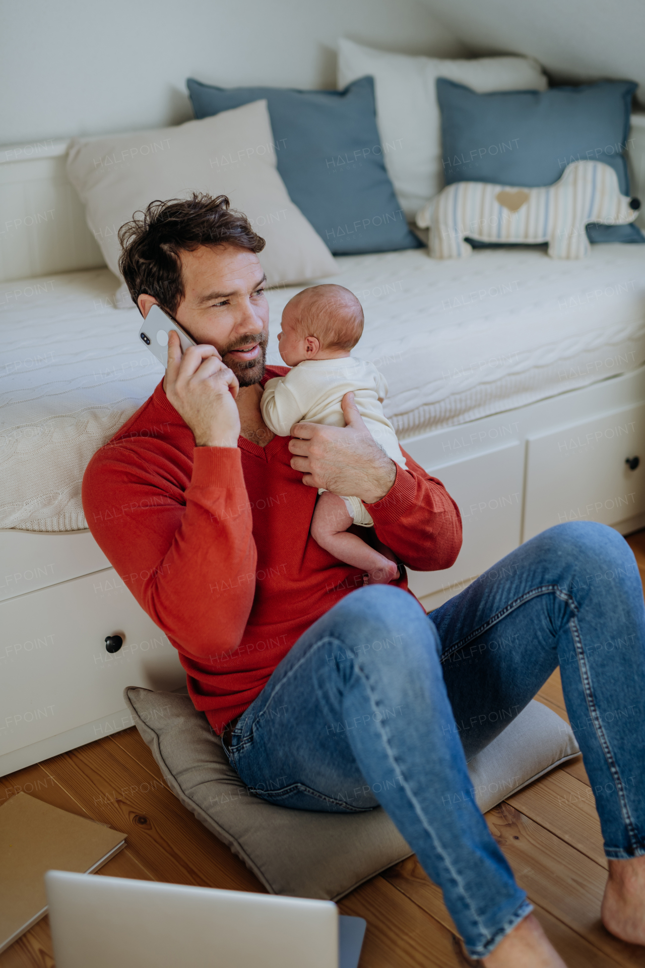 Father holding his newborn crying baby during working on a laptop.