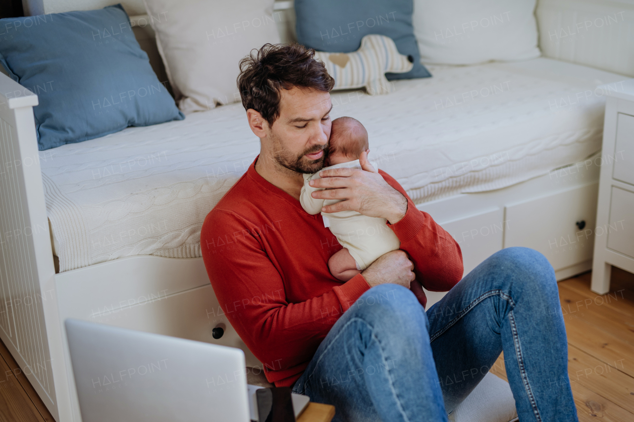 Father holding his newborn crying baby during working on a laptop.