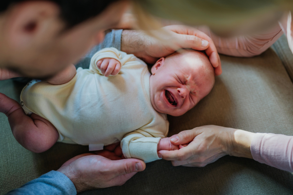 Close-up of parents cuddling their newborn crying son.