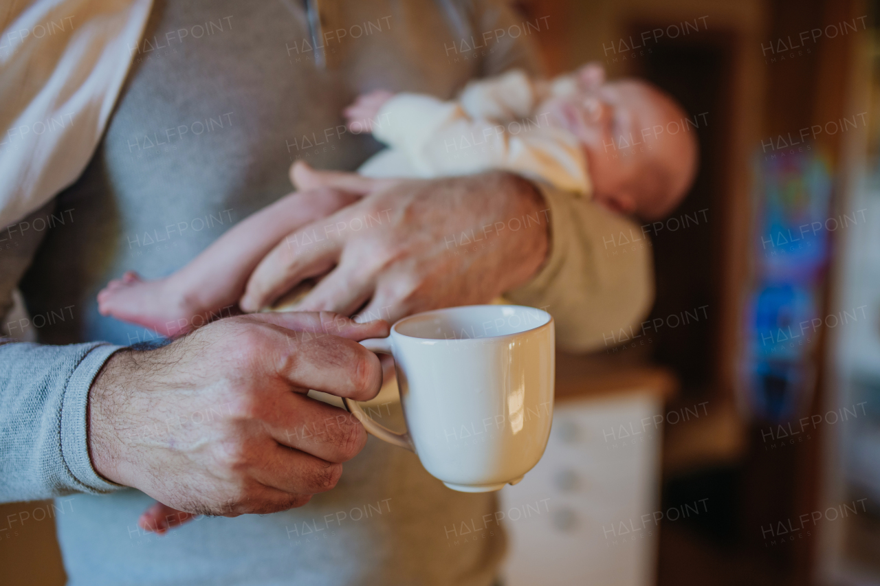 Close- up of father holding her newborn baby and a cup of coffee.