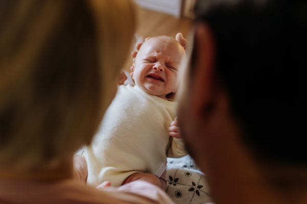 Close-up of parents cuddling their newborn crying son.