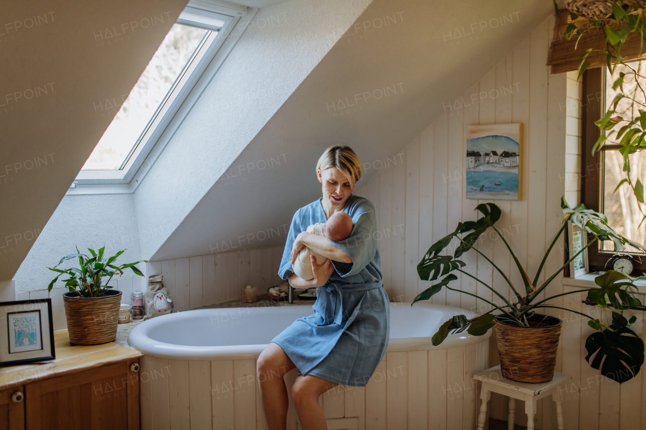 Mother cuddling her little newborn baby in their bathroom.