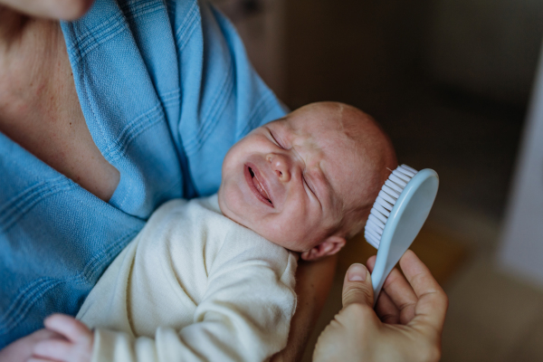 Close-up of mother combing her little newborn baby with a hair brush.