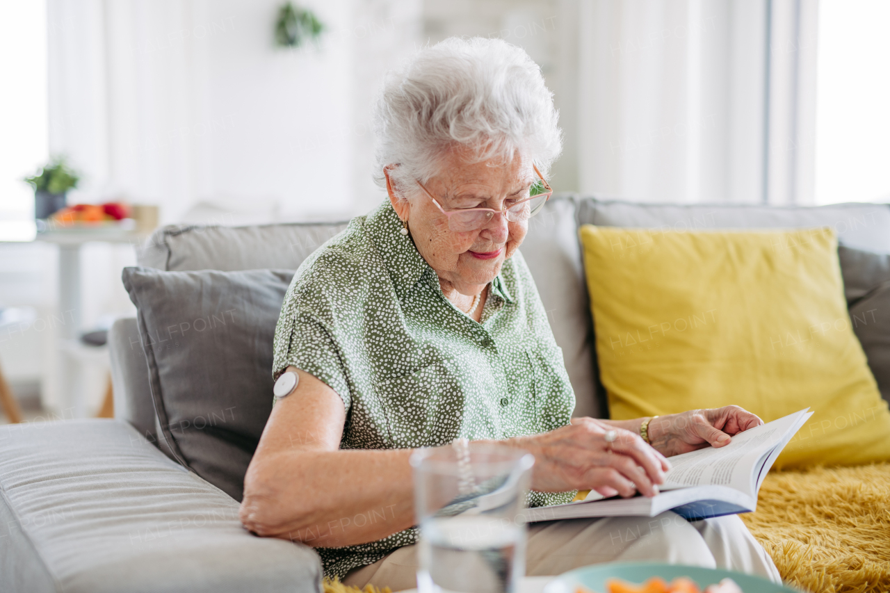 Diabetic senior patient using continuous glucose monitor to check blood sugar level at home. Senior woman drinking water to better manage her diabetes. CGM device making life of elderly woman easier.