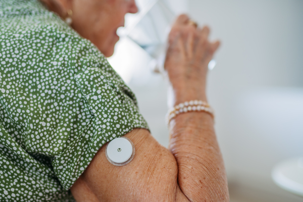 Diabetic senior patient using continuous glucose monitor to check blood sugar level at home. Senior woman drinking water to better manage her diabetes. CGM device making life of elderly woman easier.