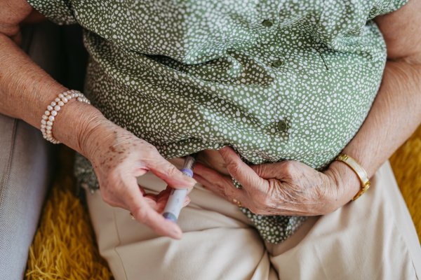 Diabetic senior patient injecting insulin in her belly. Close up of senior woman with type 1 diabetes taking insuling with syringe needle.