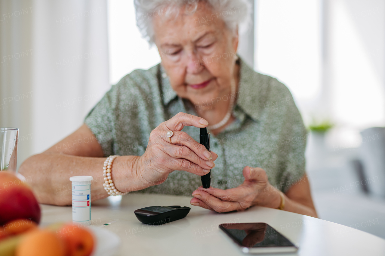 Diabetic senior patient checking her blood sugar level with fingerstick testing glucose meter. Portrait of senior woman with type 1 diabetes using blood glucose monitor at home.