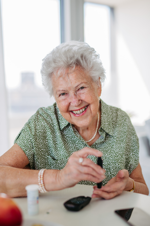 Portrait of diabetic senior patient checking her blood sugar level with fingerstick testing glucose meter. Portrait of senior woman with type 1 diabetes using blood glucose monitor at home.