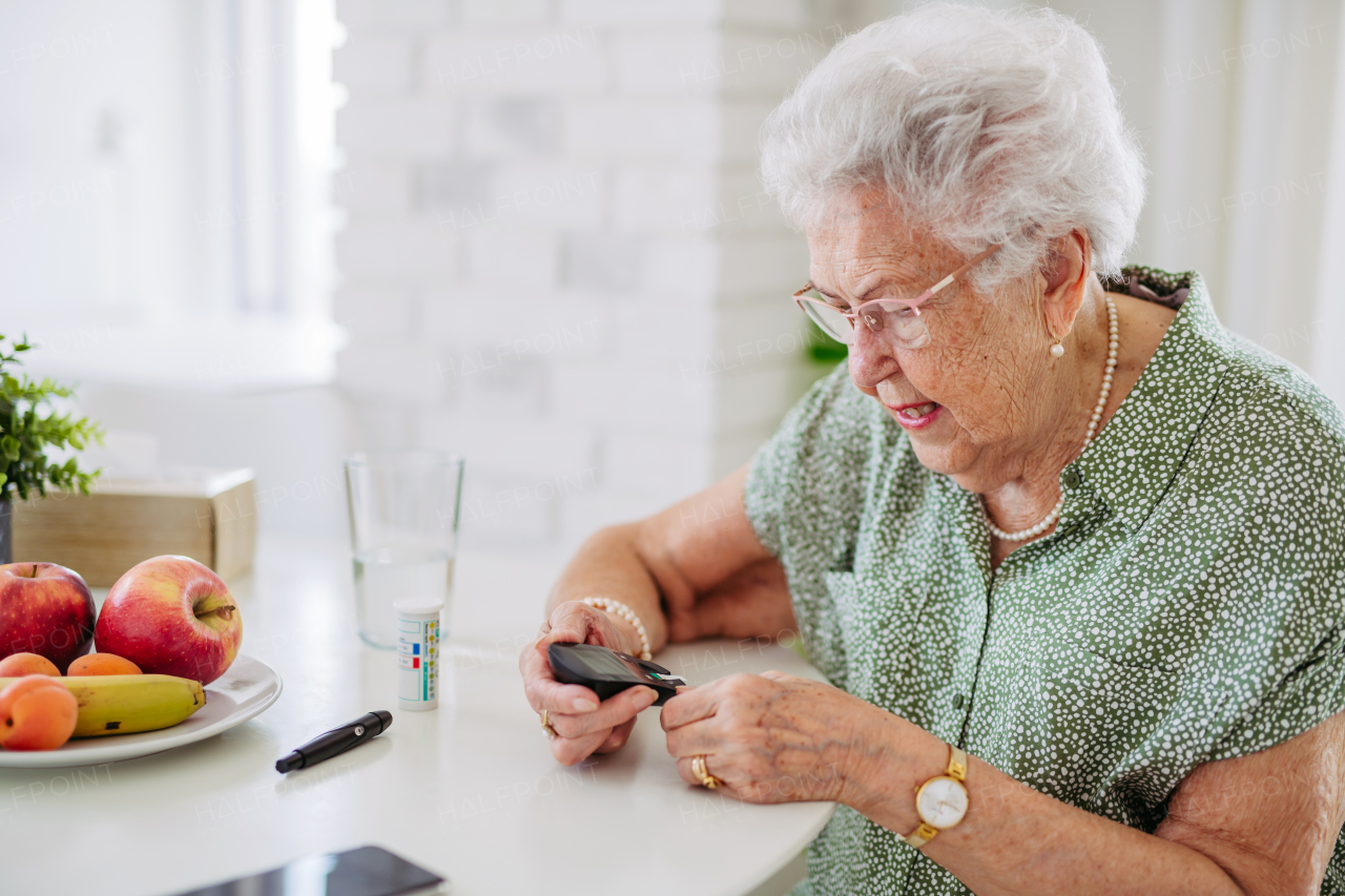 Diabetic senior patient checking her blood sugar level with fingerstick testing glucose meter. Portrait of senior woman with type 1 diabetes using blood glucose monitor at home.