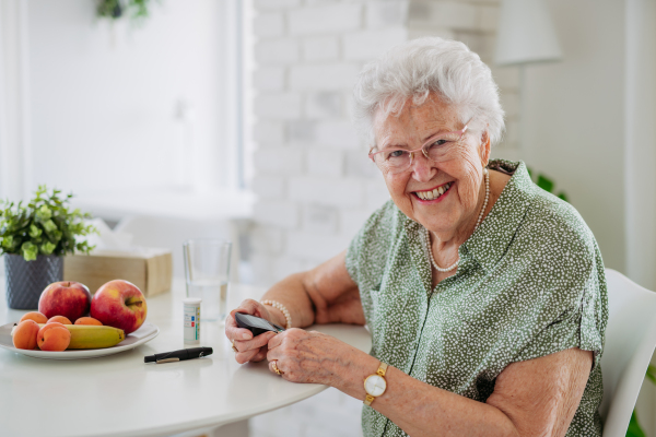 Portrait of diabetic senior patient checking her blood sugar level with fingerstick testing glucose meter. Portrait of senior woman with type 1 diabetes using blood glucose monitor at home.