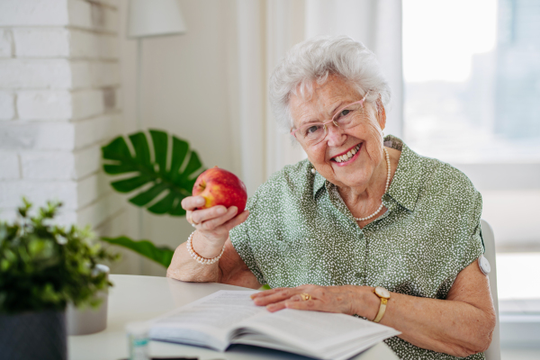 Diabetic senior patient using continuous glucose monitor to check blood sugar level at home. Senior woman eating apple to help raise her blood sugar to normal. CGM device making life of elderly woman easier, helping manage her illness and focus on other activities.