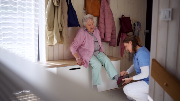 Home caregiver helping elderly woman to put on shoes. Help from nurse in daily activities for senior people.