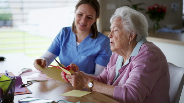 Nurse, in-home caregiver doing arts and crafts with a senior woman, cutting out paper hearts. Crafting as a fun activity for the elderly woman, helps with motor skills and emotional well-being.a