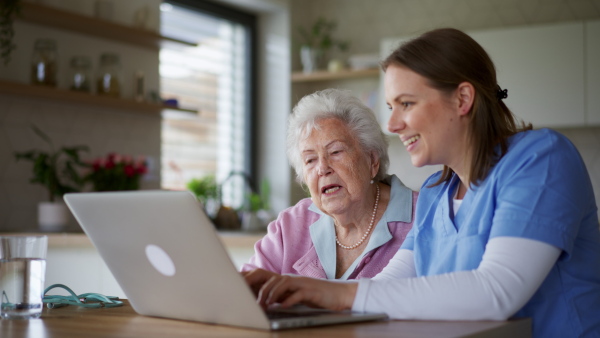 Nurse, caregiver helping senior woman to manage her finance, teaching how to work with laptop and shopping online. Technology and digital literacy for elderly person.