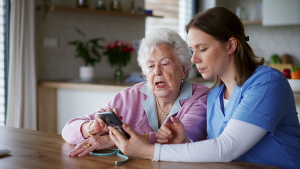 Nurse, caregiver teaching senior woman to work with smartphone and shopping online. Technology and digital literacy for elderly person.