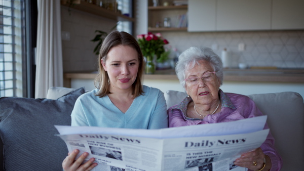 A mature daughter and elderly mother spending time together during weekend, reading newspapers and talking about news.