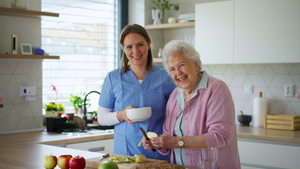 Home caregiver and elderly woman cutting apples, making healthy quick snack. Household chores for senior woman, help from nurse.