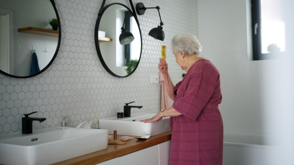 Elderly woman in bathroom, combing her hair. Senior woman at nursing home.