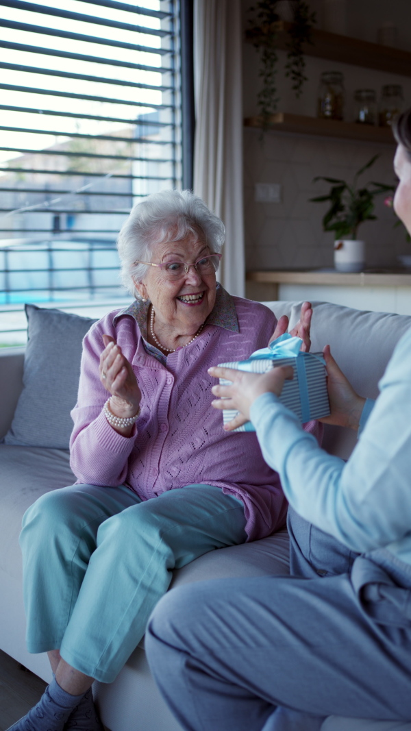 Elderly woman receiving gift for mothers day, feeling surprised and happy. Senior woman at home is thankful for wrapped birthday present.