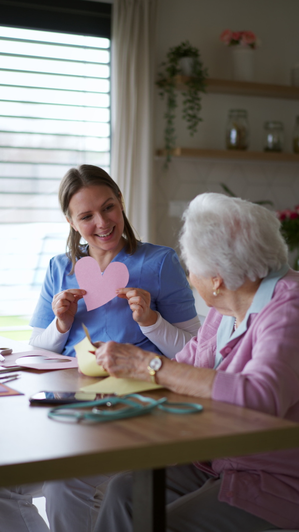 Nurse, in-home caregiver doing arts and crafts with a senior woman, cutting out paper hearts. Crafting as a fun activity for the elderly woman, helps with motor skills and emotional well-being.a