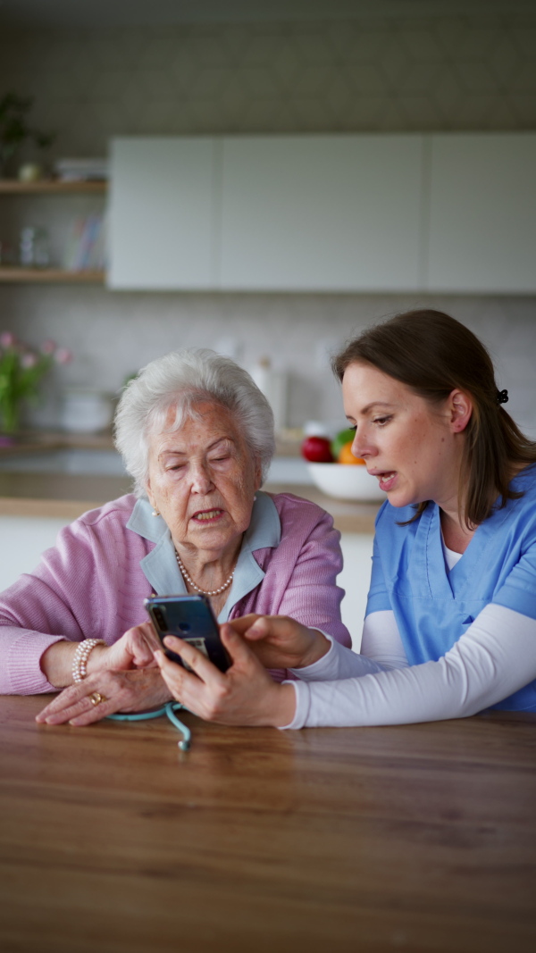 Nurse, caregiver teaching senior woman to work with smartphone and shopping online. Technology and digital literacy for elderly person.