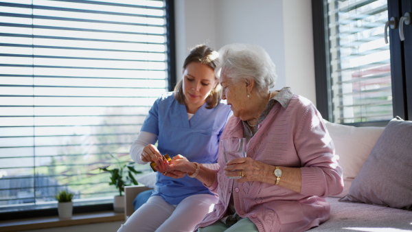 Nurse giving elderly woman a prescribed medication. Senior female patient recovering after surgery, home caregiver helping with medication administration.