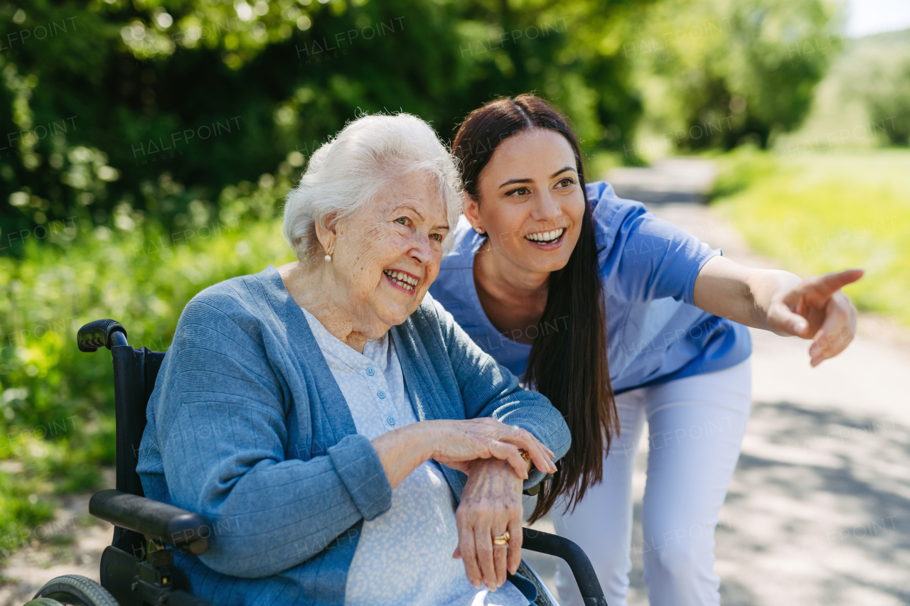 Caregiver pushing senior woman in wheelchair. Nurse and elderly woman enjoying a warm day in nursing home, public park.