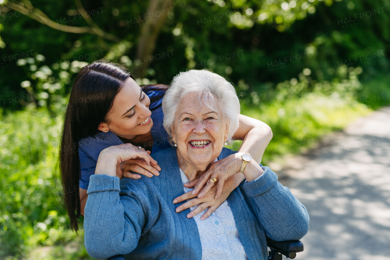 Caregiver pushing senior woman in wheelchair. Nurse and elderly woman enjoying a warm day in nursing home, public park.