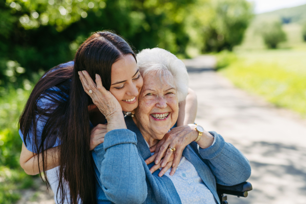 Caregiver pushing senior woman in wheelchair. Nurse and elderly woman enjoying a warm day in nursing home, public park.