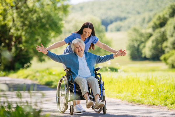 Caregiver pushing senior woman in wheelchair. Nurse and elderly woman enjoying a warm day in nursing home, public park.