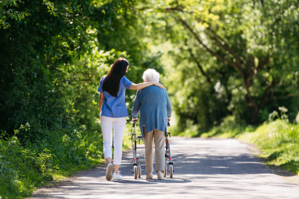 Caregiver pushing senior woman in wheelchair. Nurse and elderly woman enjoying a warm day in nursing home, public park.