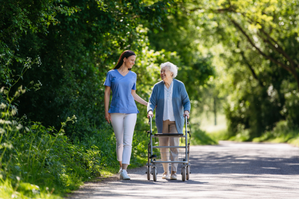 Caregiver pushing senior woman in wheelchair. Nurse and elderly woman enjoying a warm day in nursing home, public park.