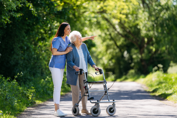 Caregiver pushing senior woman in wheelchair. Nurse and elderly woman enjoying a warm day in nursing home, public park.