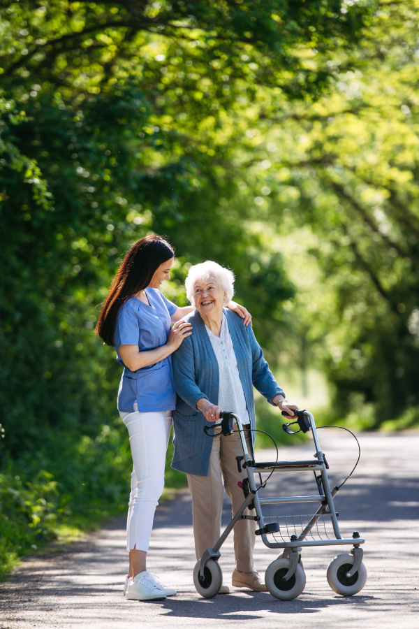 Caregiver pushing senior woman in wheelchair. Nurse and elderly woman enjoying a warm day in nursing home, public park.