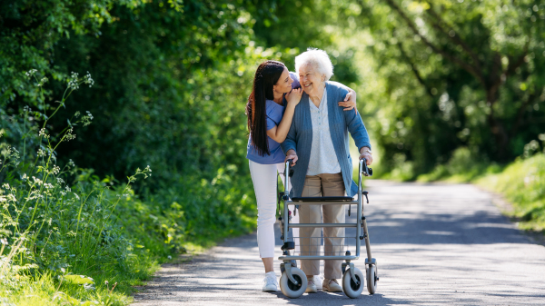 Caregiver pushing senior woman in wheelchair. Nurse and elderly woman enjoying a warm day in nursing home, public park.