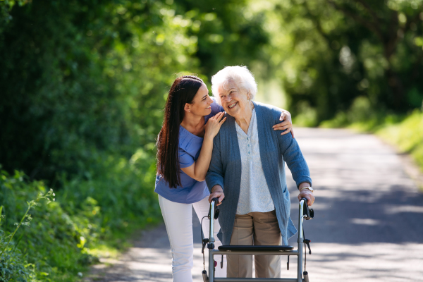 Caregiver pushing senior woman in wheelchair. Nurse and elderly woman enjoying a warm day in nursing home, public park.