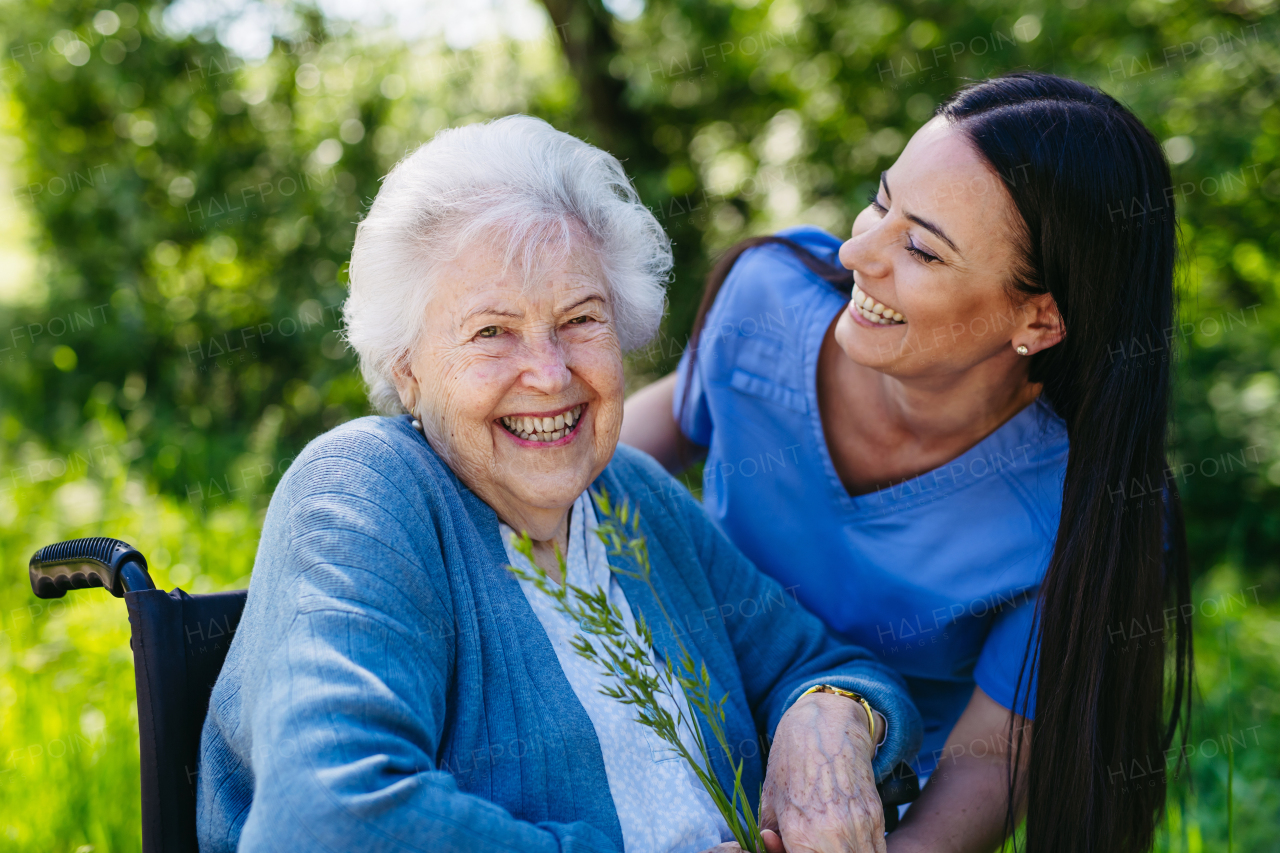 Female caregiver and senior woman in wheelchair. Nurse and elderly woman enjoying outdoor stroll during warm day in nature.