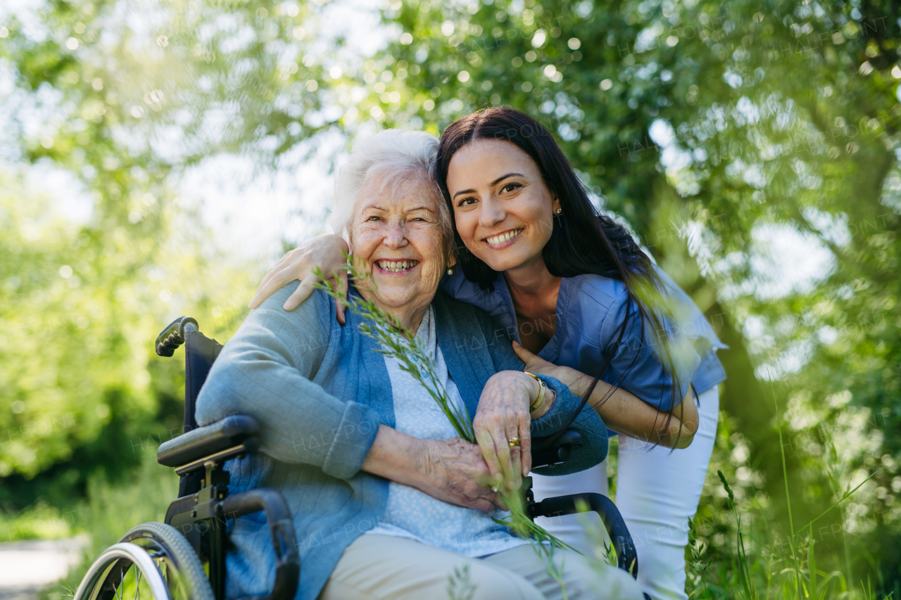 Female caregiver and senior woman in wheelchair. Nurse and elderly woman enjoying outdoor stroll during warm day in nature.