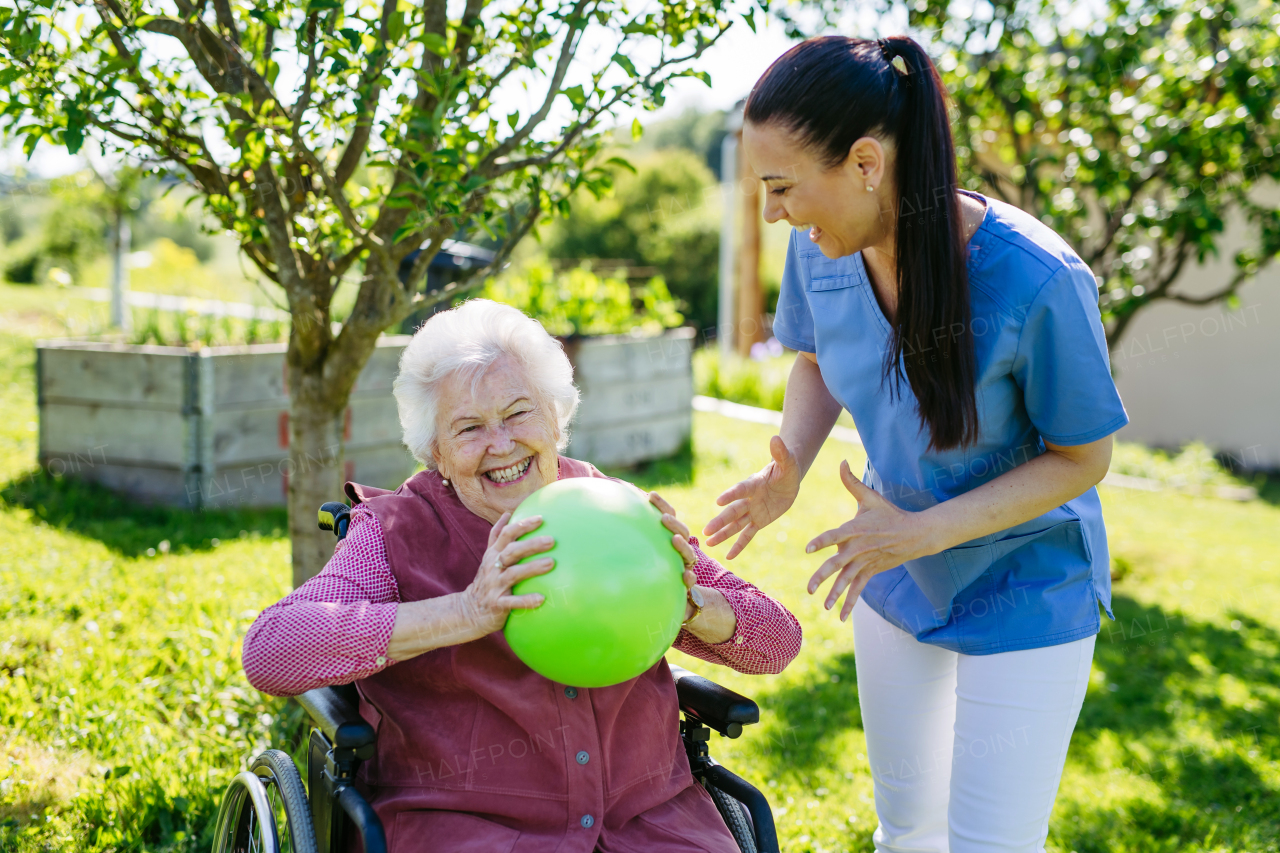 Female caregiver doing motorized exercises with senior woman in wheelchair. Nurse and elderly woman working out with green exercise ball.