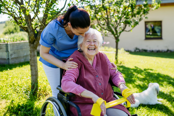 Female caregiver doing motorized exercises with senior woman in wheelchair. Nurse and elderly woman working out with yellow resistance band.