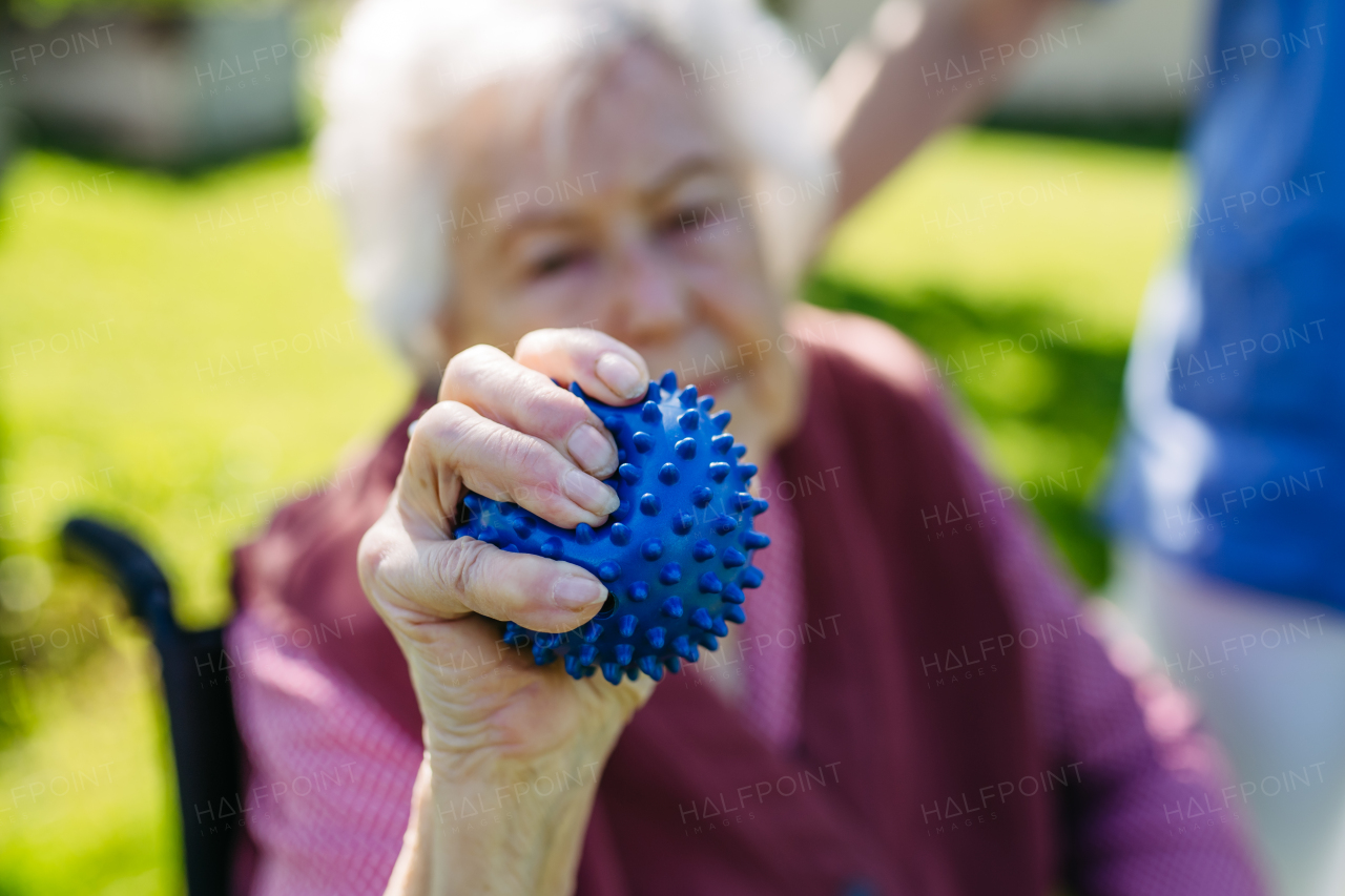 Female caregiver doing motorized exercises with senior woman in wheelchair. Nurse and elderly woman squeezing small soft ball.