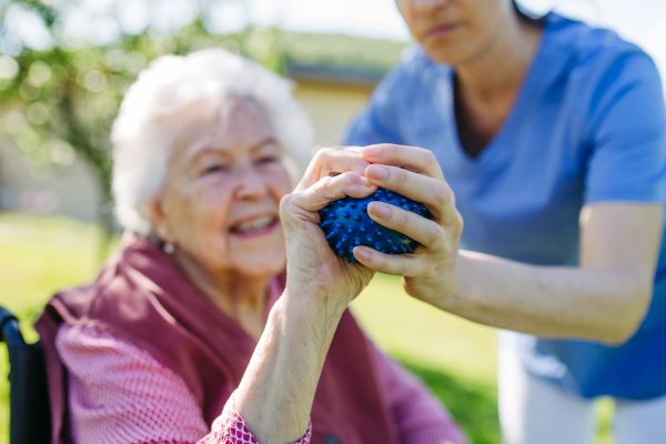 Female caregiver doing motorized exercises with senior woman in wheelchair. Nurse and elderly woman squeezing small soft ball.