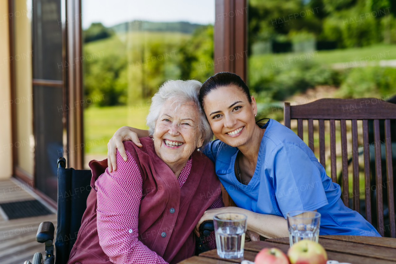 Portrait of female caregiver and senior woman embracing. Nurse and elderly woman enjoying a warm day in nursing home, public park.