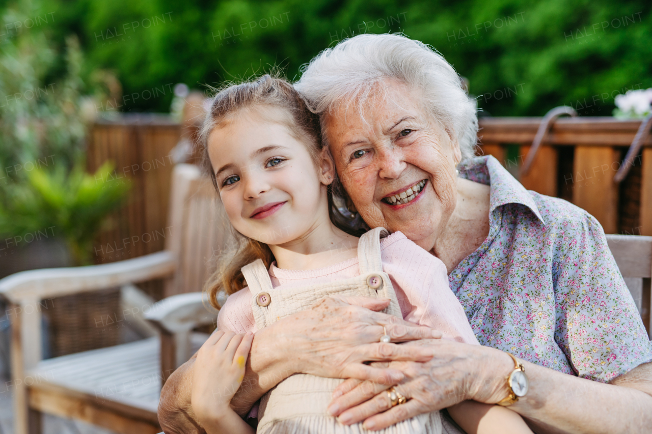 Portrait of granddaughter on patio with elderly grandma. Senior lady spending time with young girl, enjoying together time.