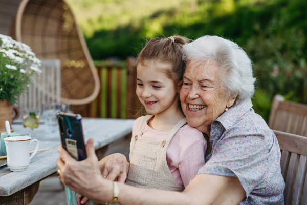 Granddaughter taking selfie with elderly grandma, companionship. Senior lady spending time with young girl, enjoying together time. Weekend in cottage.