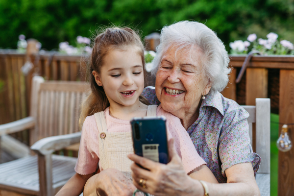 Granddaughter taking selfie with elderly grandma, companionship. Senior lady spending time with young girl, enjoying together time. Weekend in cottage.