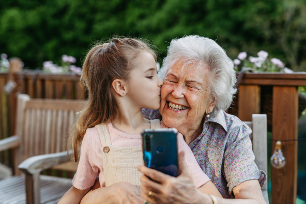 Granddaughter taking selfie with elderly grandma, companionship. Senior lady spending time with young girl, enjoying together time. Weekend in cottage.