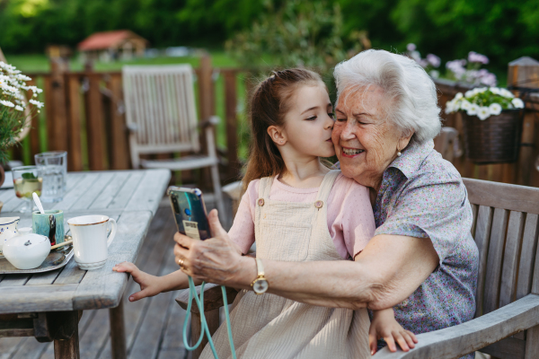 Granddaughter taking selfie with elderly grandma, companionship. Senior lady spending time with young girl, enjoying together time. Weekend in cottage.